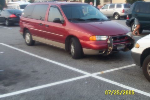 1998 Ford Crown Victoria - Three-quarter front view of a red Ford Windstar minivan with tan lower body cladding and a roof rack, parked across striped spaces in a lot…