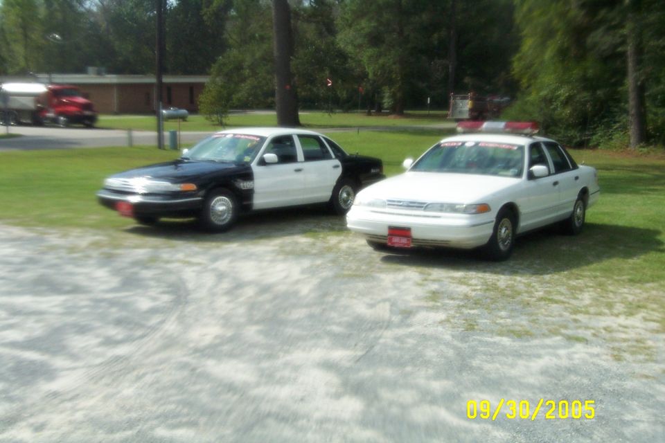1998 Ford Crown Victoria police car in white parked next to a black and white police car