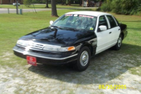 1998 Ford Crown Victoria - A black and white 1998 Ford Crown Victoria, marked as 'Fire Rescue', is parked outdoors on a sunny day.