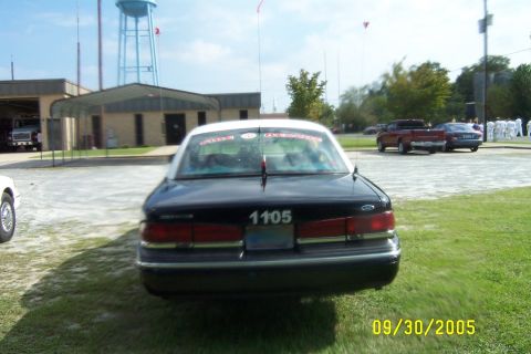 1998 Ford Crown Victoria - A black and white sedan is parked in front of a fire station with a water tower in the background.