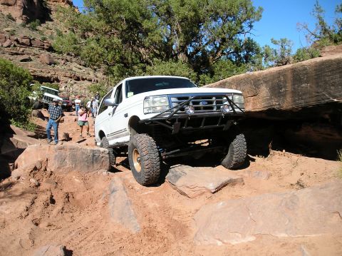 1993 Ford Bronco - A white 1993 Ford Bronco tackles a challenging off-road trail with other vehicles visible in the background.