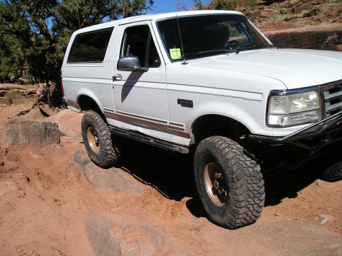 1993 Ford Bronco - White 1993 Ford Bronco tackles a challenging off-road trail with large rocks.