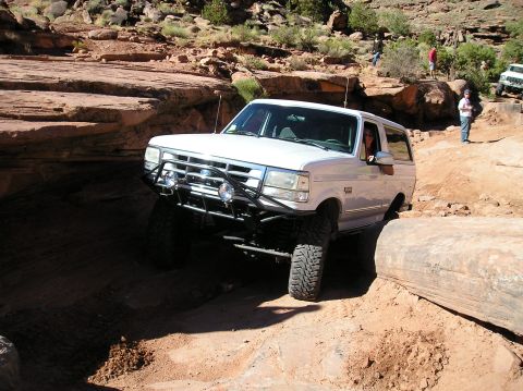 1993 Ford Bronco - A white Ford Bronco maneuvers through a challenging off-road course with spectators present.