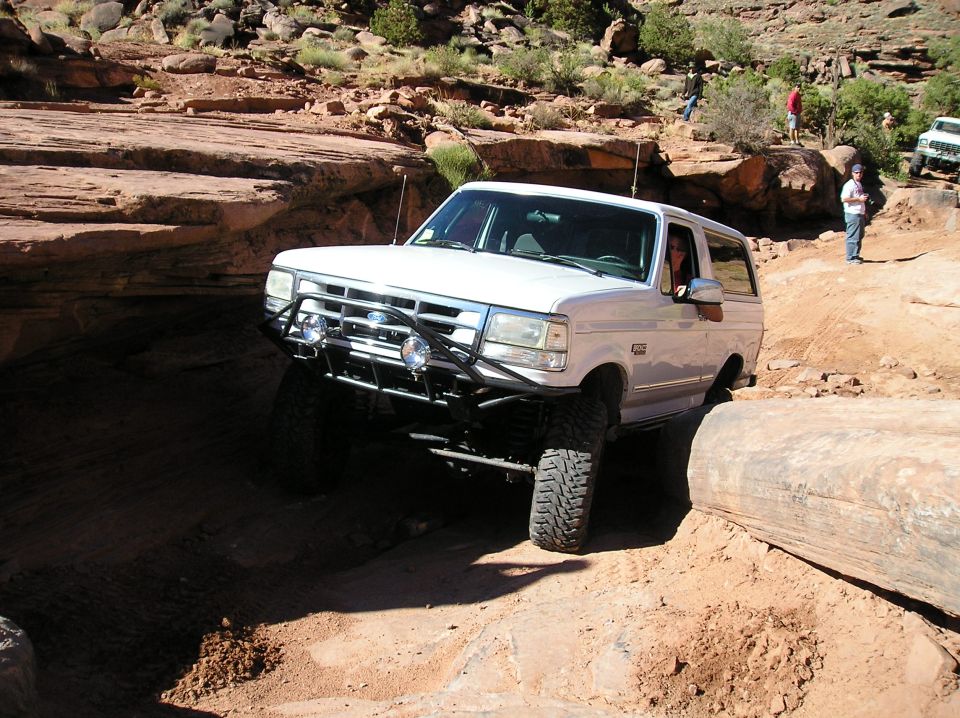 White Ford Bronco navigating a rocky off-road trail, with people watching