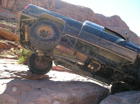 1993 Ford Bronco - A black pickup truck navigates challenging terrain, tilted precariously on large rocks.
