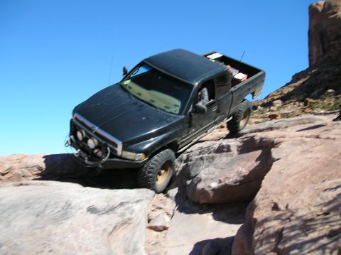 1993 Ford Bronco - A black pickup truck is shown off-roading on a rocky trail under a clear blue sky.