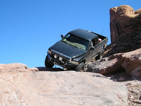 1993 Ford Bronco - Pickup truck navigates a rocky trail under a clear blue sky.