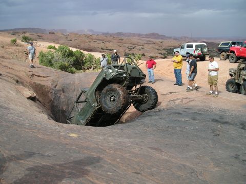 1993 Ford Bronco - An off-road vehicle is precariously stuck in a deep crevice on a rocky terrain, with onlookers observing the scene.