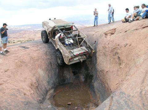 1993 Ford Bronco - An off-road vehicle navigates a challenging obstacle on a rocky terrain with spectators watching.