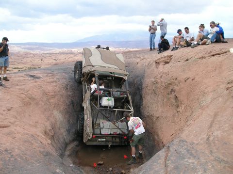1993 Ford Bronco - Spectators observe an off-road vehicle carefully maneuver down a steep, narrow rock formation in a desert landscape.