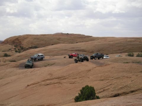 1993 Ford Bronco - Multiple off-road vehicles are gathered on a large rock formation in a desert environment.