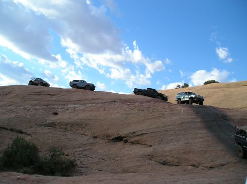 1993 Ford Bronco - Several off-road vehicles navigate a steep, rocky terrain on a sunny day.
