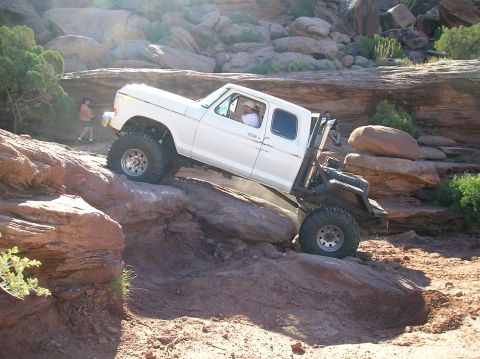 1993 Ford Bronco - A modified pickup truck navigates a rocky trail in a desert landscape.