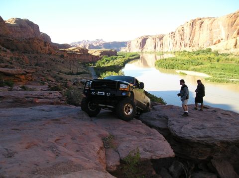 1993 Ford Bronco - A lifted black Ford F-250 Super Duty truck is parked on a rocky ledge next to a river.