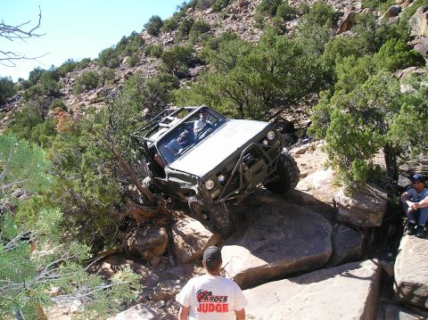 1993 Ford Bronco - Modified off-road vehicle attempts to traverse difficult rocky terrain on a sunny day.