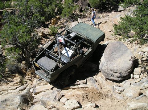 1993 Ford Bronco - A modified off-road vehicle navigates a challenging rocky trail, with a person observing from higher ground.