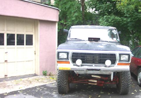 1978 Ford Bronco - This lifted Ford Bronco features a distinctive grille and front end, parked next to a garage with a red car visible on the side.