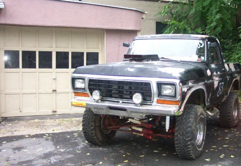 1978 Ford Bronco - This modified Ford F-Series truck features a lifted suspension and a prominent hood scoop, parked outside a garage.