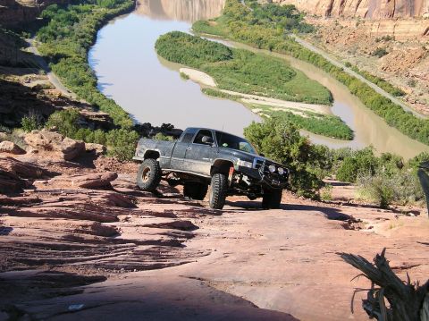 1993 Ford Bronco - Pickup truck navigates challenging rocky terrain with a river and canyon in the background.
