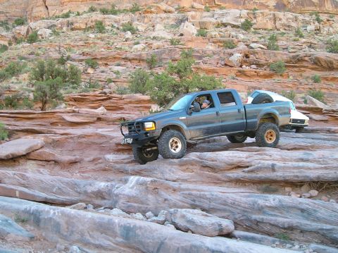 1993 Ford Bronco - Ford F-Series pickup navigates rocky terrain in a desert landscape, with another vehicle following.
