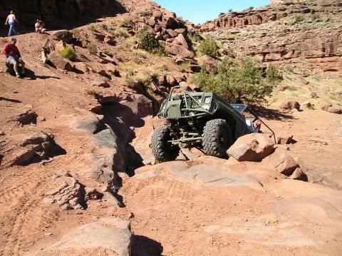 1993 Ford Bronco - A heavily modified off-road vehicle tackles a challenging rocky trail in a desert landscape.