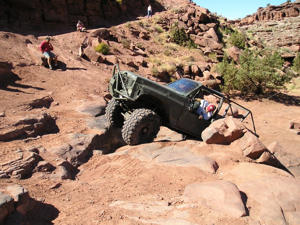 Olive green off-road vehicle with roll cage navigating rocky terrain