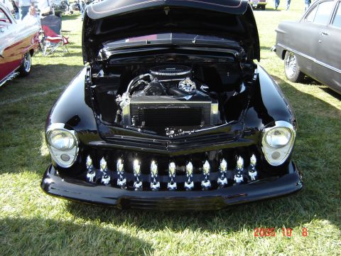 1993 Ford Bronco - A black custom car with its hood open is displayed on a grassy field next to other vehicles.