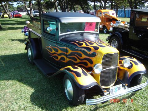 1993 Ford Bronco - A vintage hot rod pickup truck with flame graphics is parked on grass at an outdoor event.