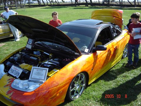 1993 Ford Bronco - A custom coupe with flame graphics and an open hood is displayed on a grassy field.