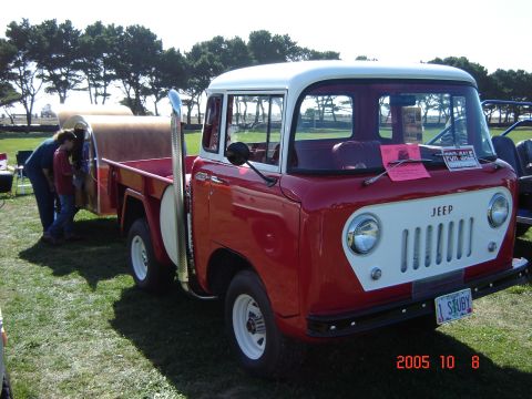 1993 Ford Bronco - A classic red and white Jeep pickup truck is parked on a grassy field with trees in the background.