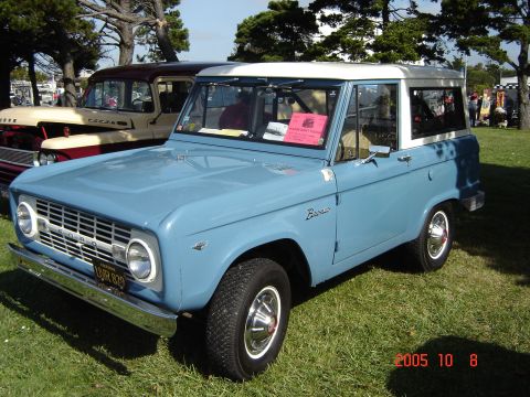 1993 Ford Bronco - A classic blue Ford Bronco is parked on a grassy field next to another vintage vehicle.