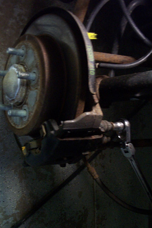 1999 Chrysler 300M - Close-up of a vehicle's disk brake assembly, showing the rotor, caliper, and a wrench in use.