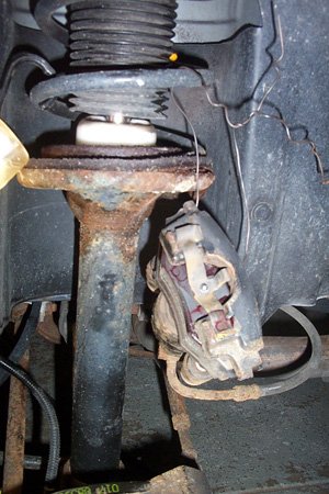 1999 Chrysler 300M - Rusty brake caliper and strut assembly, likely from a car's suspension system.