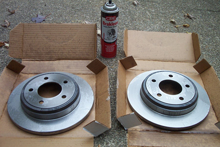 1999 Chrysler 300M - Two new brake rotors and a can of brake cleaner are laid out on a concrete surface.