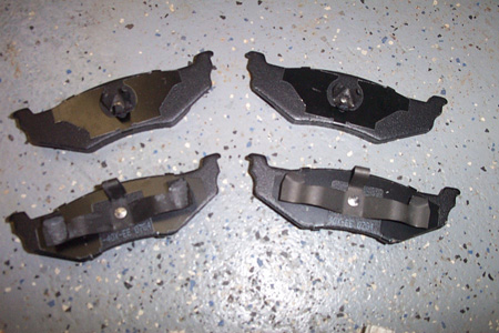 1999 Chrysler 300M - A set of four brake pads are shown on a garage floor. The part number is partially visible.