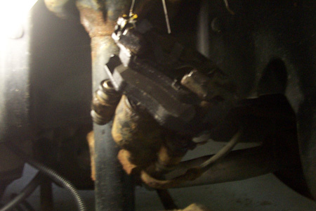 1999 Chrysler 300M - A close-up view of a vehicle's disk brake caliper and rotor assembly, showing signs of rust and wear.