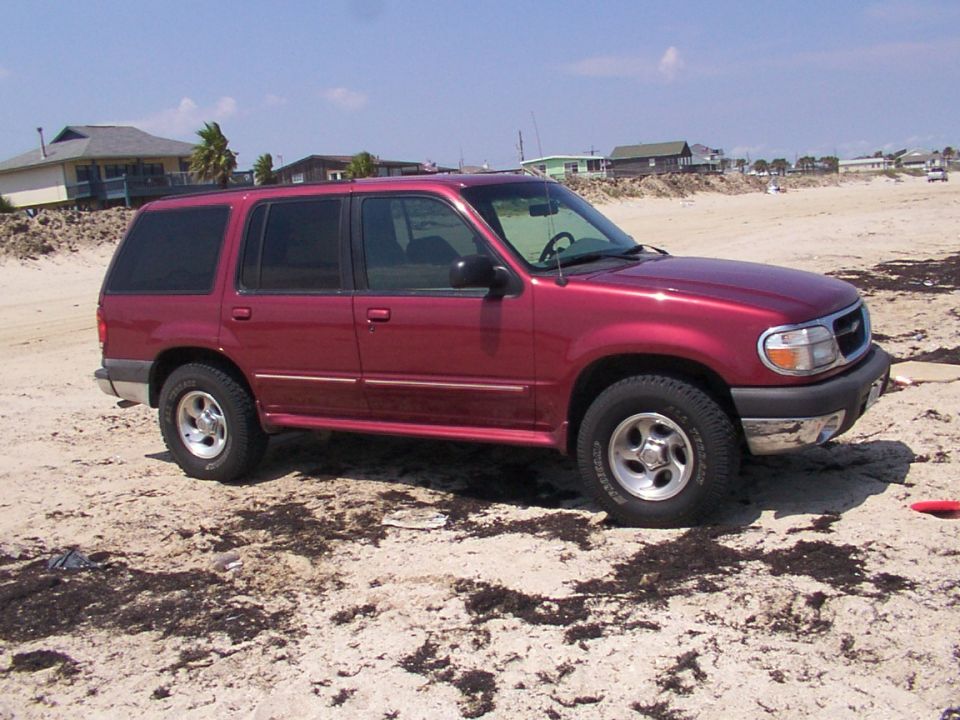 Maroon Ford Explorer SUV parked on a sandy beach, passenger-side front three-quarter view