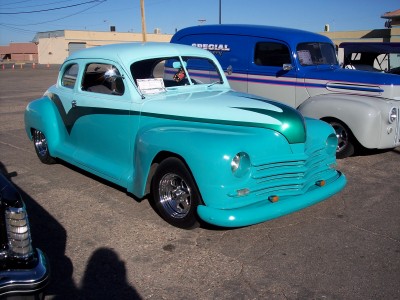1972 Ford Ranchero - A custom teal coupe with a two-tone paint job and chrome wheels is parked outdoors next to a blue van.