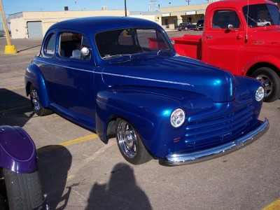 1972 Ford Ranchero - A blue 1946 Ford coupe hot rod is parked next to a red pickup truck.