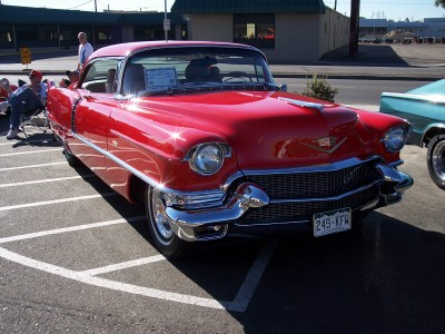 1972 Ford Ranchero - A bright red 1955 Cadillac Coupe de Ville is parked at an outdoor event, its distinctive grille and chrome accents gleaming.