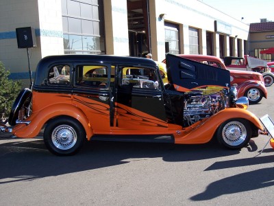 1972 Ford Ranchero - A custom hot rod with flame graphics and an open hood displaying its engine is parked alongside other vehicles.