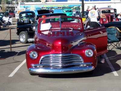 1972 Ford Ranchero - A shiny red convertible is parked at a car show, with its door open and other vehicles in the background.