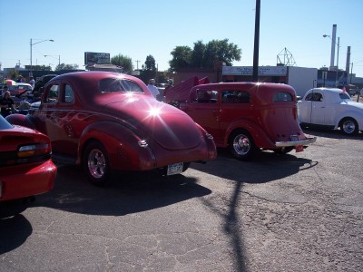 1972 Ford Ranchero - Two red classic cars, a coupe and a sedan, are parked outdoors on a sunny day.