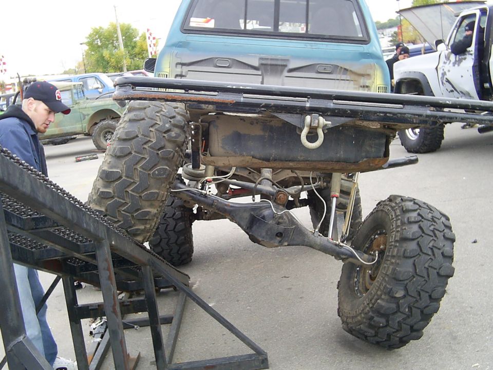 Off-road truck rear axle and suspension with large tires, another truck in background