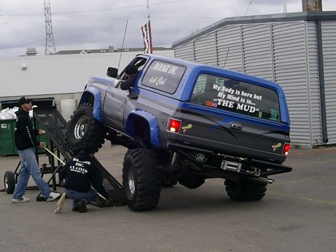 1985 Ford Bronco - A modified 1985 Ford Bronco, lifted and equipped with large off-road tires, is positioned on a ramp at an event.