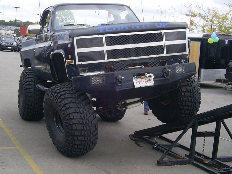 Lifted black pickup truck with large tires and a custom bumper. Blue text on the hood reads 'TEAR IT UP'. License plate PVK-686 is visible