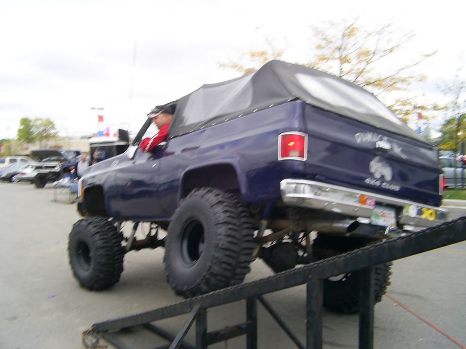 Purple lifted SUV with a soft top, driving up a ramp, with "Damage Inc 4x4 Club" decal on the rear