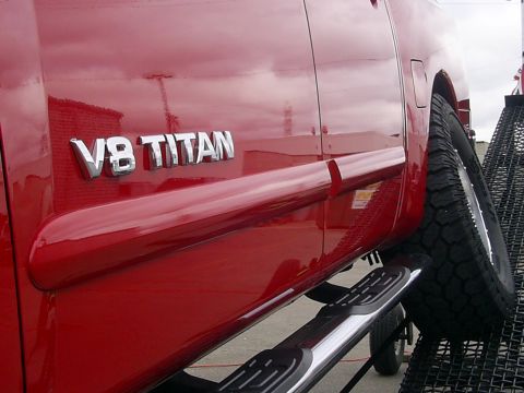 1985 Ford Bronco - Close-up of a red truck's side, showing the 'V8 TITAN' badging and running boards.