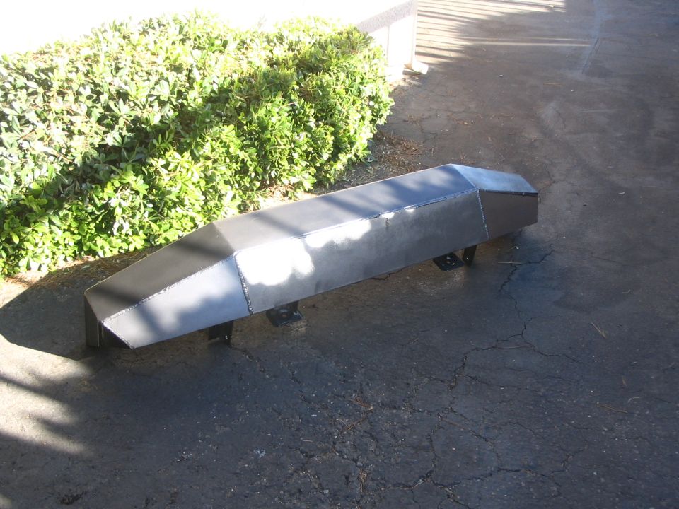 Bare welded steel tube and plate bumper lying on cracked asphalt by a hedge