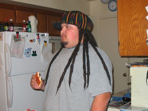 1986 Ford Bronco - A person in a gray t-shirt wearing a striped Rasta-colored cap with attached dreadlocks stands in a home kitchen holding a slice of pizza,…
